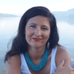 An Indigenous woman with long dark hair sits against a misty lake background.