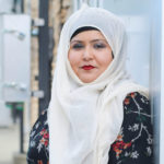 A young Muslim woman in a patterend dress and white hijab.