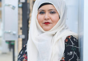 A young Muslim woman in a patterend dress and white hijab.