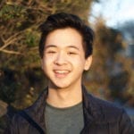 A young asian man outside wearing a grey t-shirt under a black quilted jacket