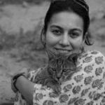 An indian woman carring a cat and wearing a floral shirt. The image is in black and white.