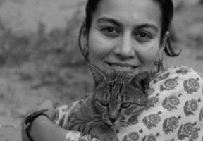 An indian woman carring a cat and wearing a floral shirt. The image is in black and white.
