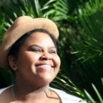 A close-up of a Black woman with her face to the sun and wearing a hat