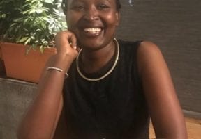 A Black woman sitting and wearing a black tank top.
