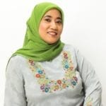 A south asian woman wearing a green hijab and a grey sweater with flowers