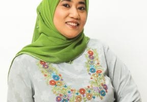 A south asian woman wearing a green hijab and a grey sweater with flowers