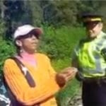 A Black woman outside wearing an orange sweater and a cap standing next to a police officer