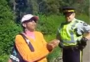 A Black woman outside wearing an orange sweater and a cap standing next to a police officer