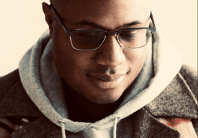 A Black man with a shaved head and glasses.
