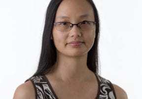 A young Asian woman wears a black and white scoop beck tank top and stands against a white background. She wears glasses.
