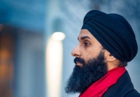 A young Indian man with a long beard and wearig a red scarf and a blackturban ;ppls pff to the left of the camera/.