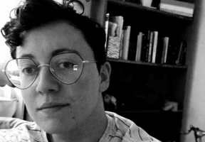 A black-and-white picture of a non-binary individual with glasses and short curly hair.