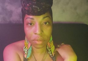 A young Black woman crosses her arms in front of her neck and looks into the camera.