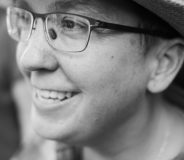 A black-and-white photo of a Latinx woman. She wears glasses and a hat with a brim.