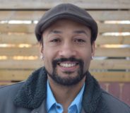 A Black man wearing a flat brown cap. He has a small goatee and smiles at the camera.