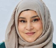 A woman with dark eyes and a beige hijab smiles at the camera.