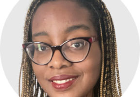 A young Black woman with long brown-blond braids and dark-rimmed glasses against a white background.