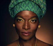 A photo of author Chidiogo Akunyili-Parr--a young Black woman wearing a gold headscarf, green dress, and glowing golden jewelry